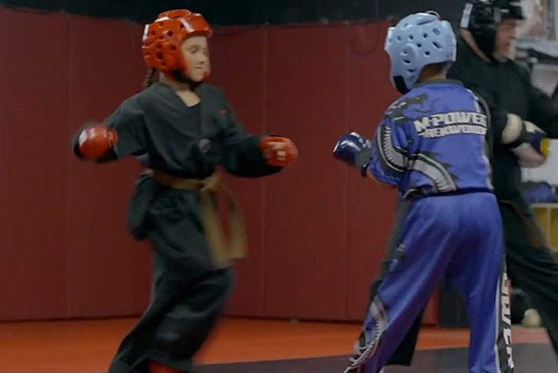 Two young students sparring in protective helmets during a taekwondo class at MPower Gym & Academy